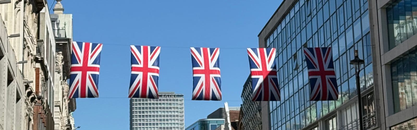 A row of United Kingdom flags are suspended by two buildings. 